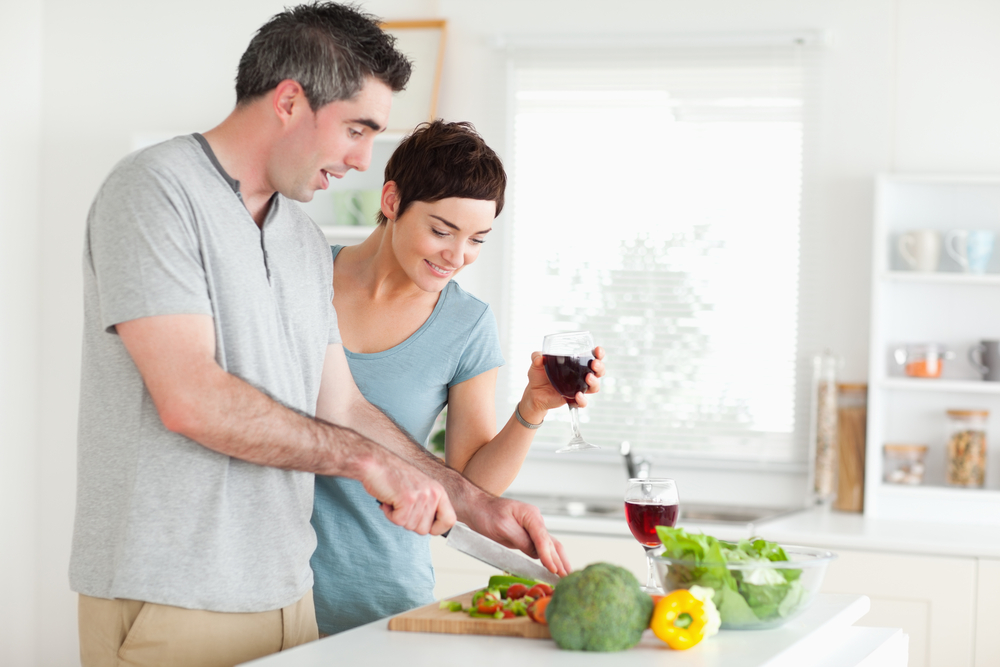 Man cutting vegetables while is woman is watching in a kitchen